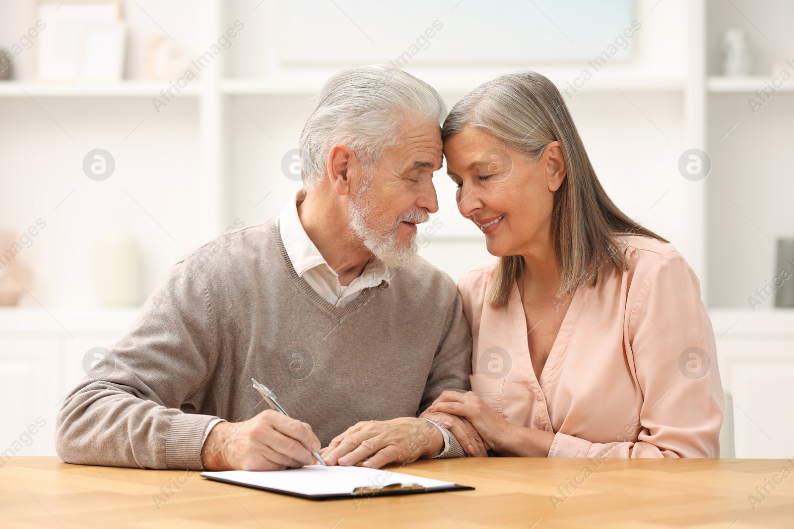 Photo of Happy senior couple signing Last Will and Testament indoors