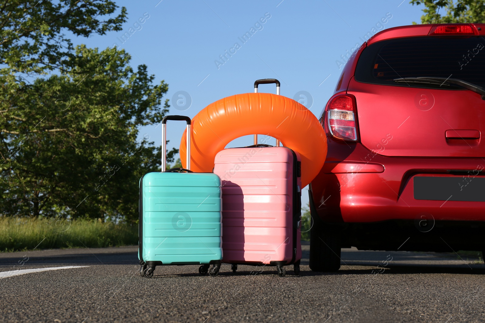 Photo of Color suitcases and inflatable ring near family car on highway. Summer vacation