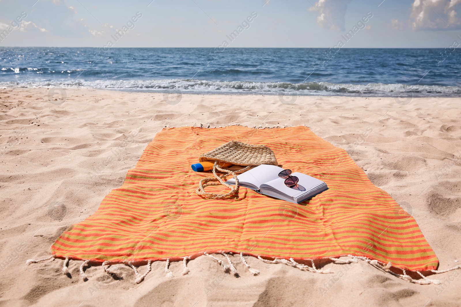 Photo of Orange striped beach towel with bag, accessories and book on sandy seashore