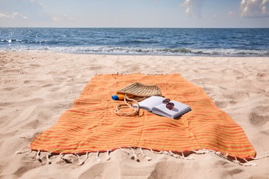 Photo of Orange striped beach towel with bag, accessories and book on sandy seashore