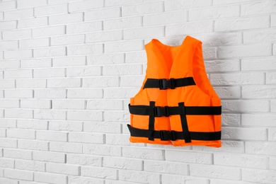 Photo of Orange life jacket on white brick wall. Space for text