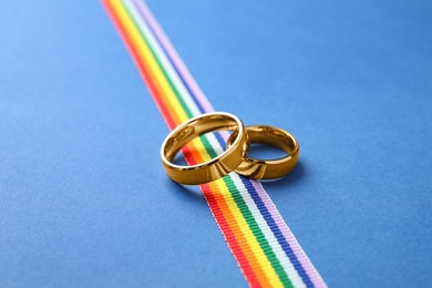 Wedding rings and rainbow ribbon on color background. Gay symbol