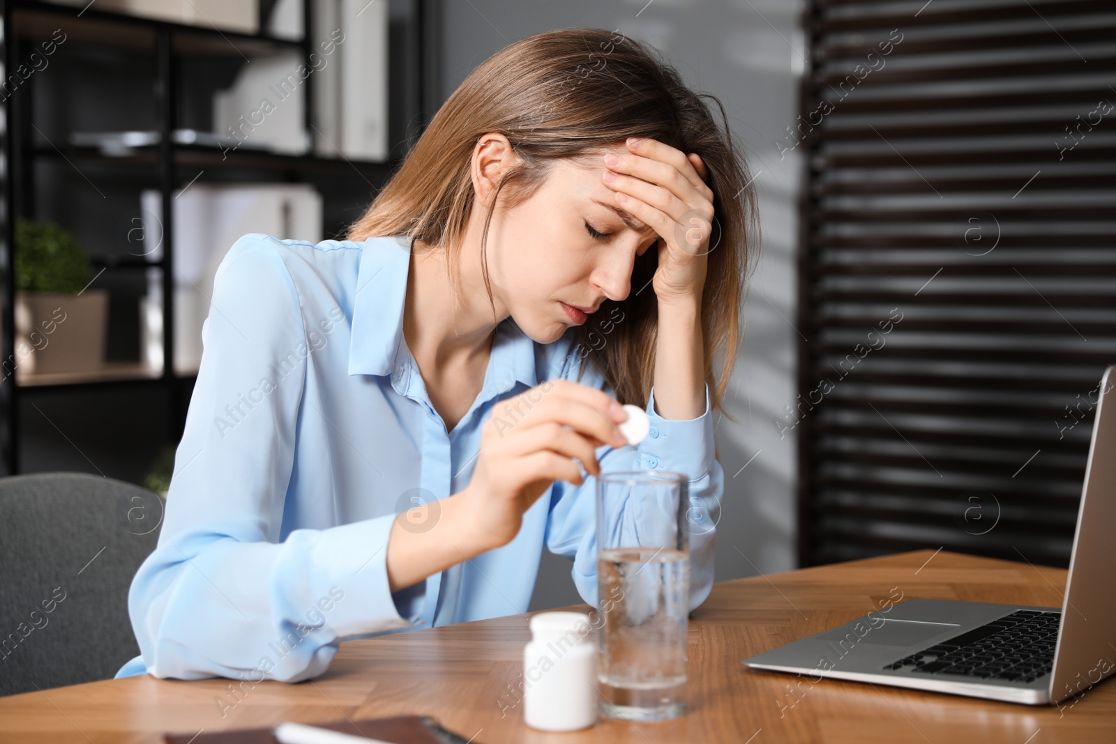 Photo of Woman putting medicine for hangover into glass of water in office