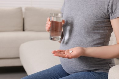 Photo of Pregnant woman with glass of water and pill at home, closeup