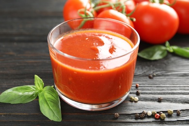 Photo of Glass of tomato sauce with basil on wooden table, closeup