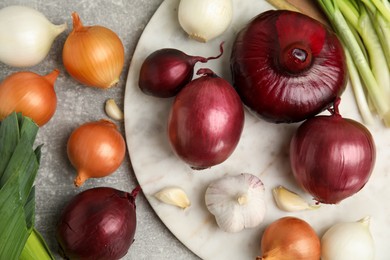 Photo of Fresh onion bulbs, leek and garlic on grey table, flat lay