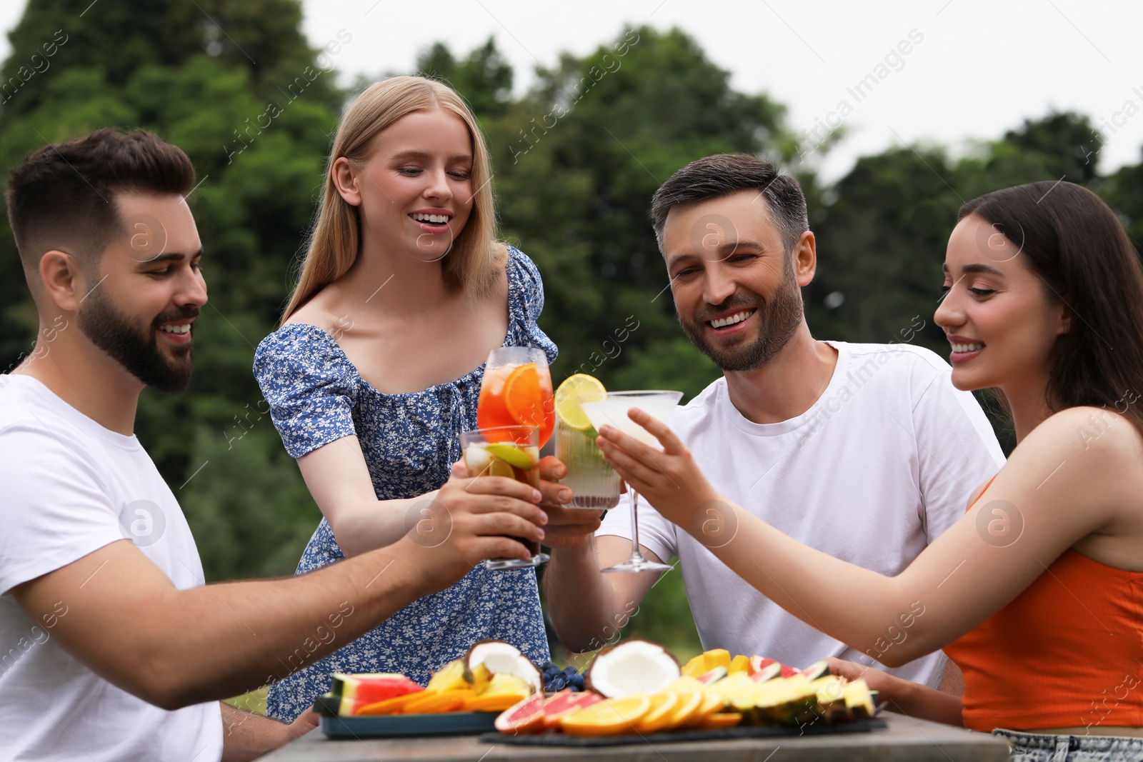 Photo of Happy friends clinking glasses with cocktails at table outdoors