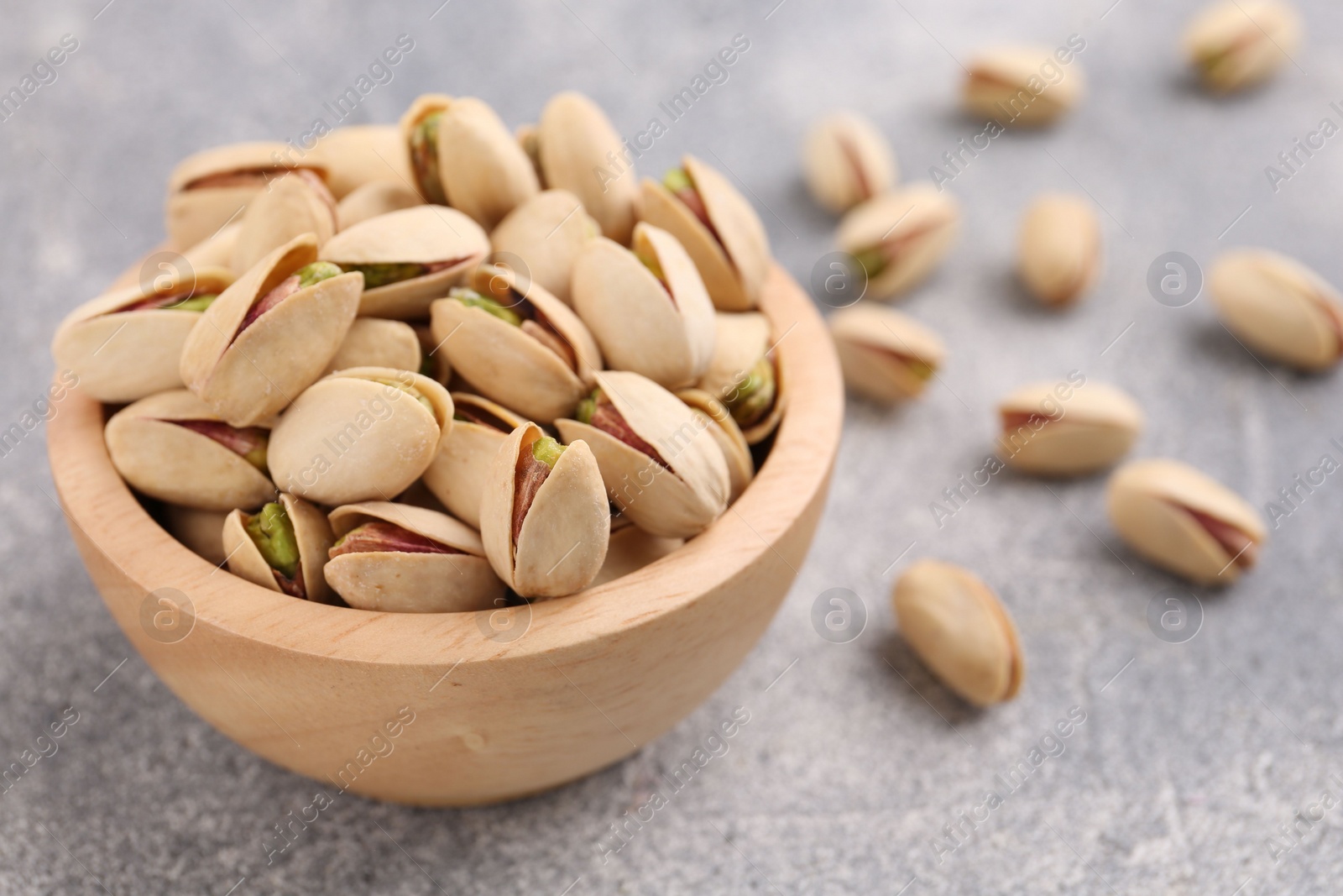 Photo of Delicious pistachios in bowl on grey textured table