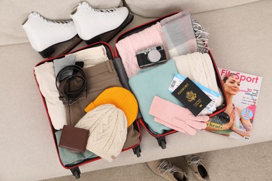 Open suitcase with warm clothes, accessories and shoes on sofa indoors, top view