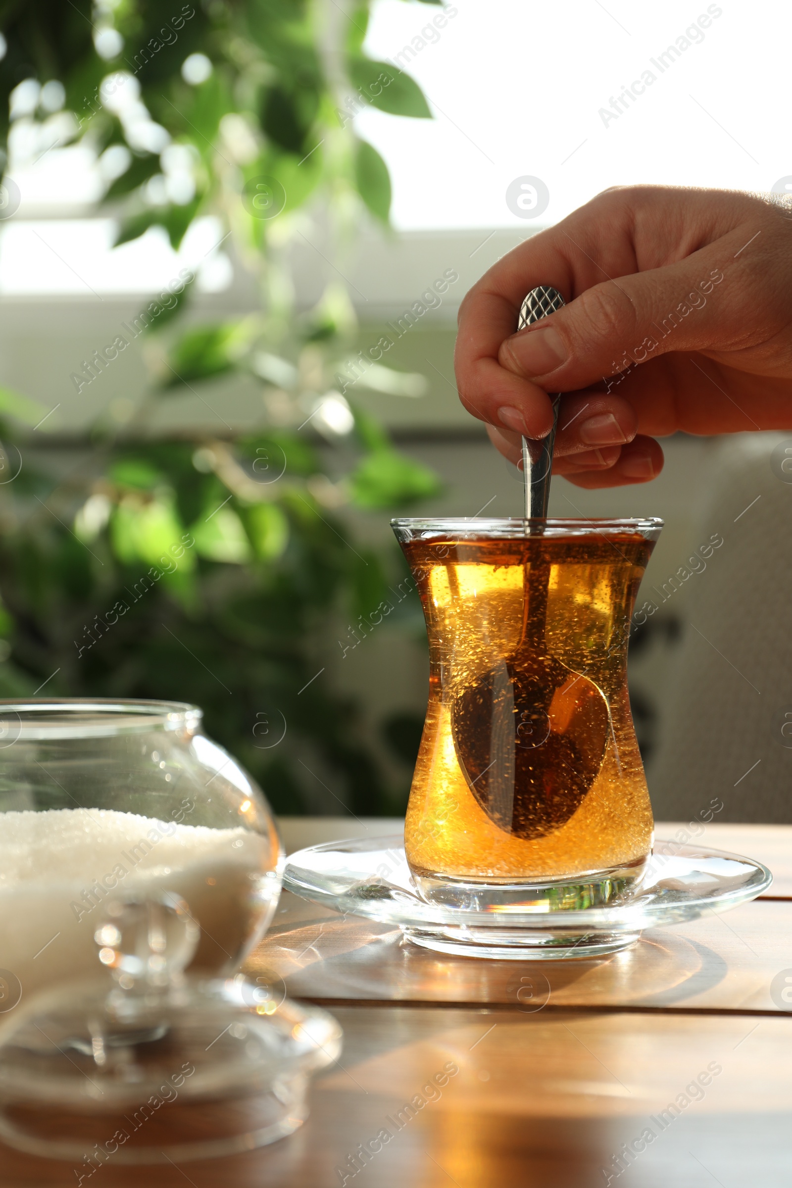 Photo of Woman stirring sugar in tea at wooden table indoors, closeup