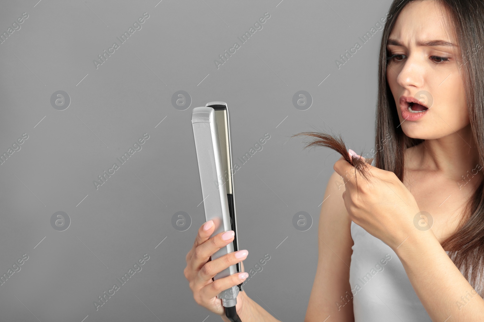 Photo of Upset woman with hair iron on grey background, space for text