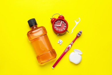 Photo of Mouthwash, toothbrush, dental floss and alarm clock on yellow background, flat lay