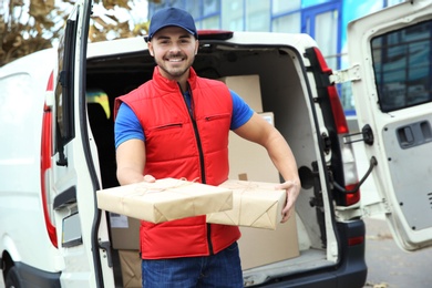 Photo of Young courier with parcels near delivery van outdoors