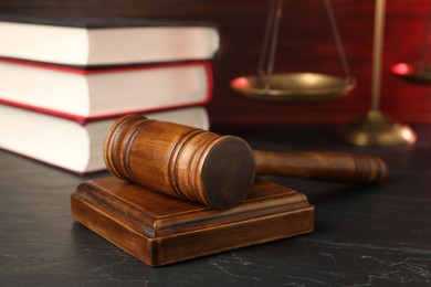 Photo of Wooden gavel, scales and stack of books on dark textured table, closeup