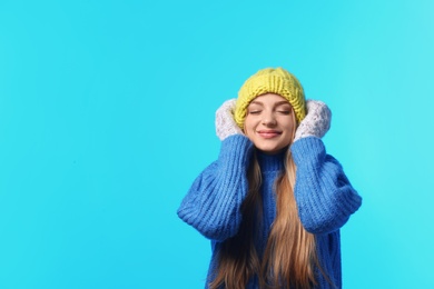 Portrait of emotional young woman in stylish hat, sweater and mittens on color background, space for text. Winter atmosphere