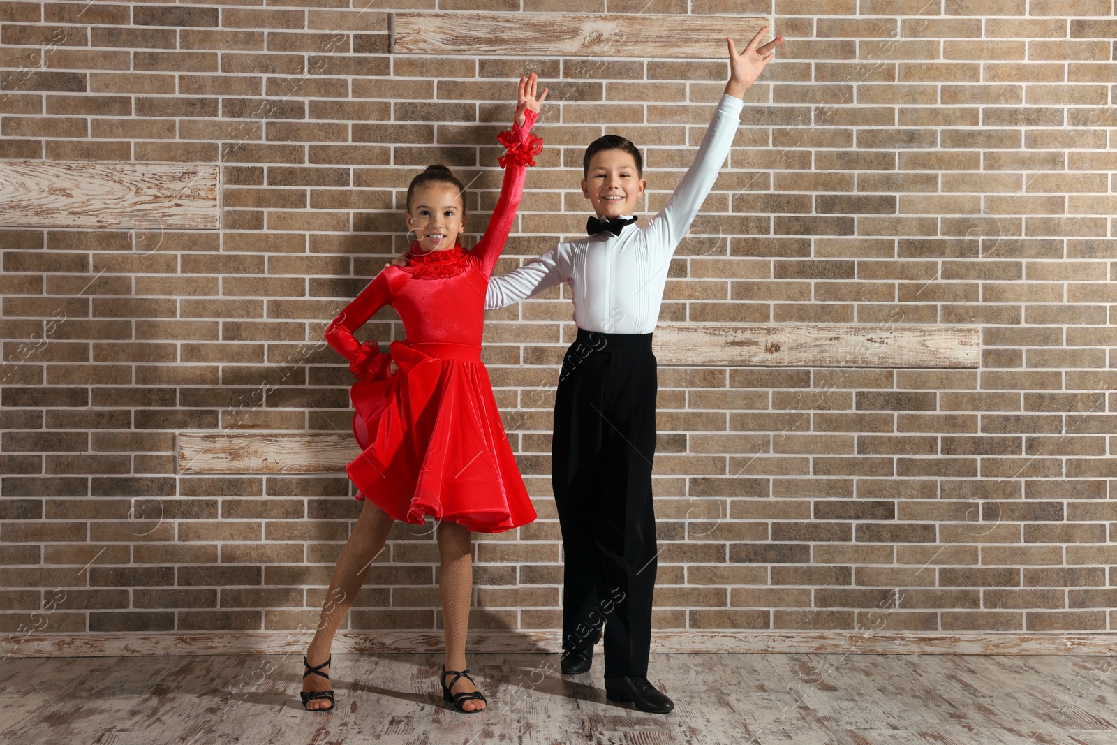 Photo of Beautifully dressed couple of kids dancing together near brick wall indoors