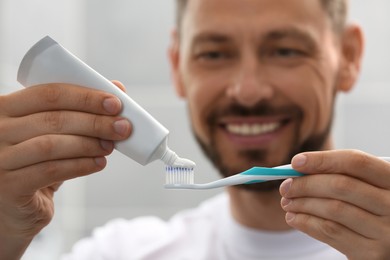 Man applying toothpaste onto brush against blurred background, focus on hands