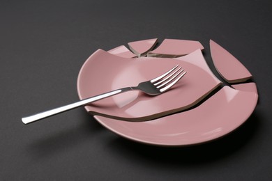 Pieces of broken ceramic plate and fork on dark grey background