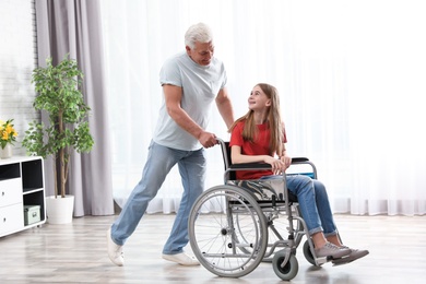 Photo of Happy grandfather and teenage girl in wheelchair at home