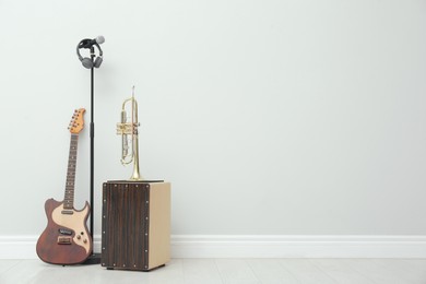 Photo of Electric guitar, trumpet and microphone near white wall indoors, space for text. Musical instruments