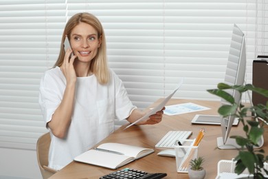 Professional accountant talking on phone while working at wooden desk in office