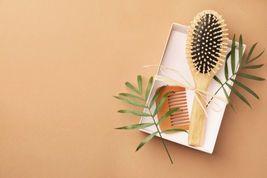 Photo of Wooden hairbrush, comb and green leaves on light brown background, top view. Space for text
