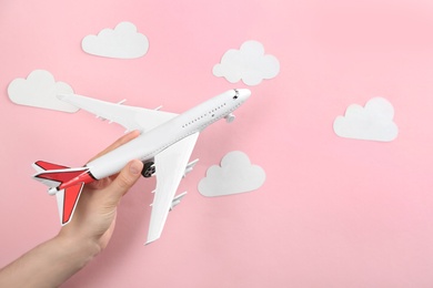 Woman holding toy airplane against pink background with clouds, closeup