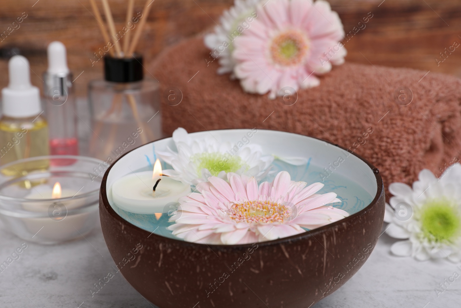 Photo of Beautiful composition with bowl of water, flowers and candles on light table, closeup. Spa treatment