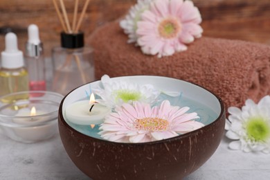 Beautiful composition with bowl of water, flowers and candles on light table, closeup. Spa treatment