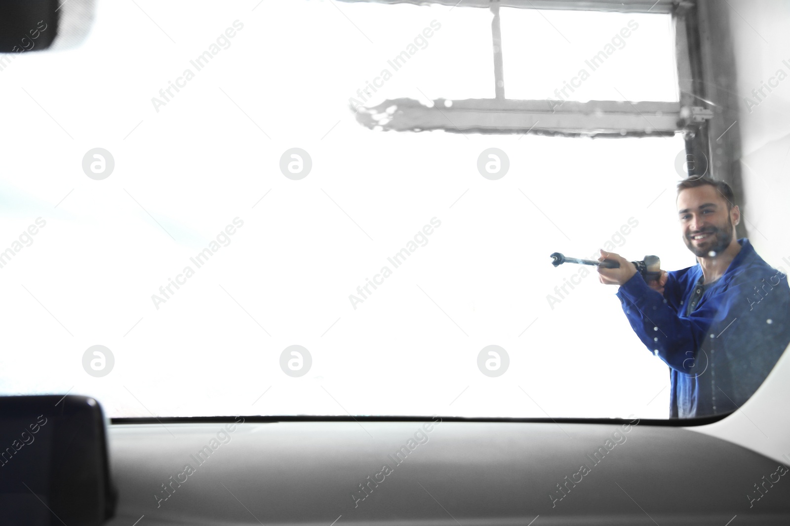 Photo of Worker cleaning automobile windshield with high pressure water jet at car wash, view from inside