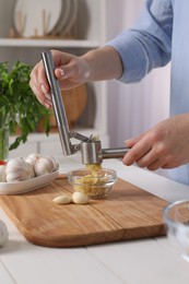 Photo of Woman squeezing garlic with press at white wooden table in kitchen, closeup