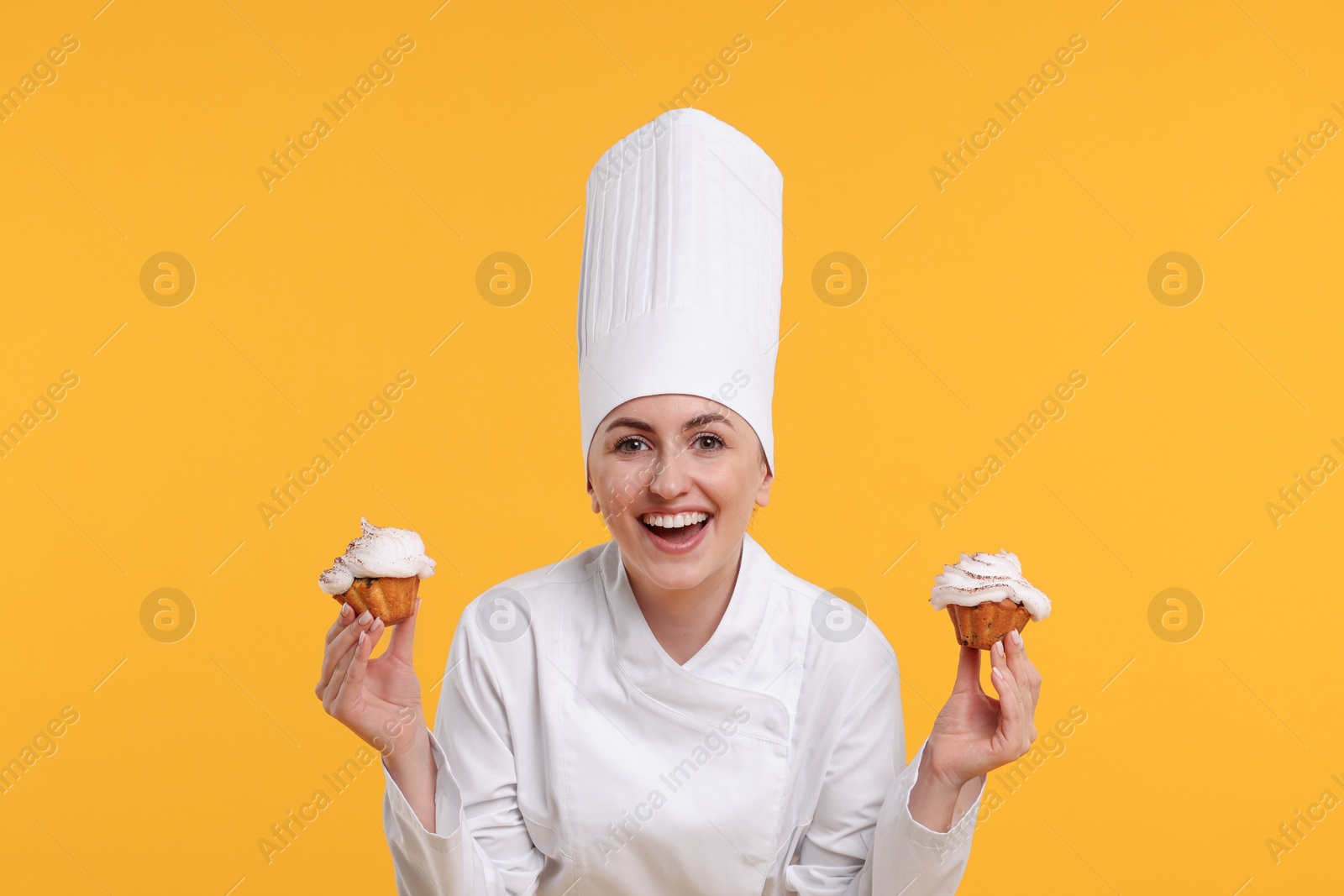 Photo of Happy professional confectioner in uniform holding delicious cupcakes on yellow background