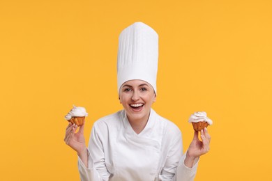 Happy professional confectioner in uniform holding delicious cupcakes on yellow background