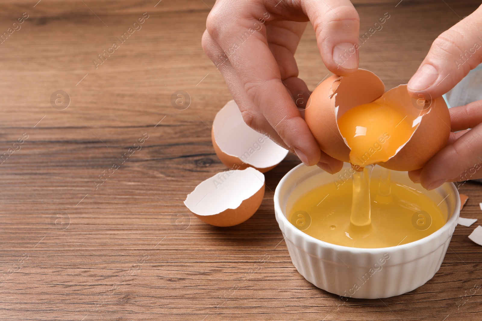 Photo of Woman separating egg yolk from white over bowl at wooden table, closeup