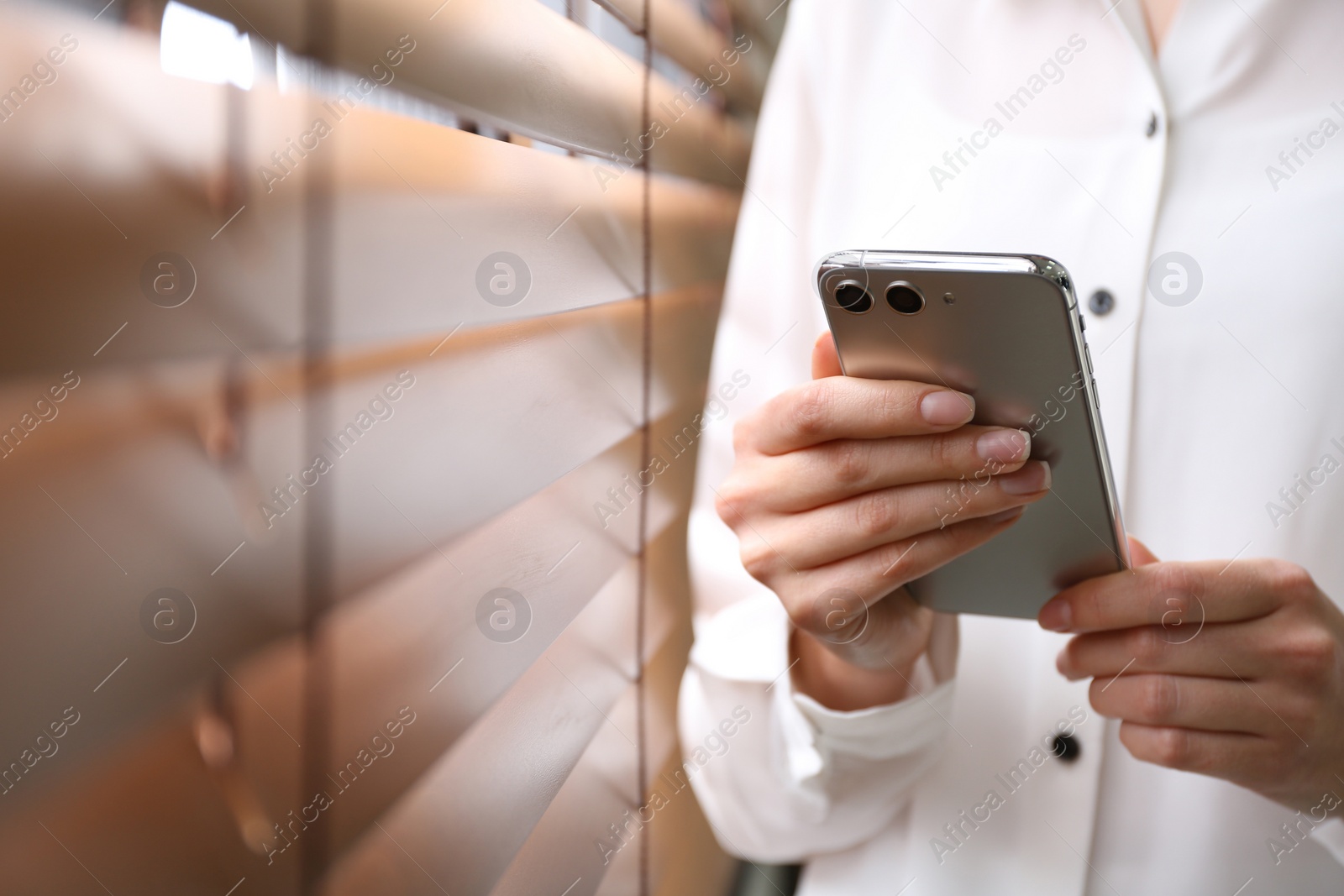 Photo of Young woman using modern smartphone near window indoors, closeup