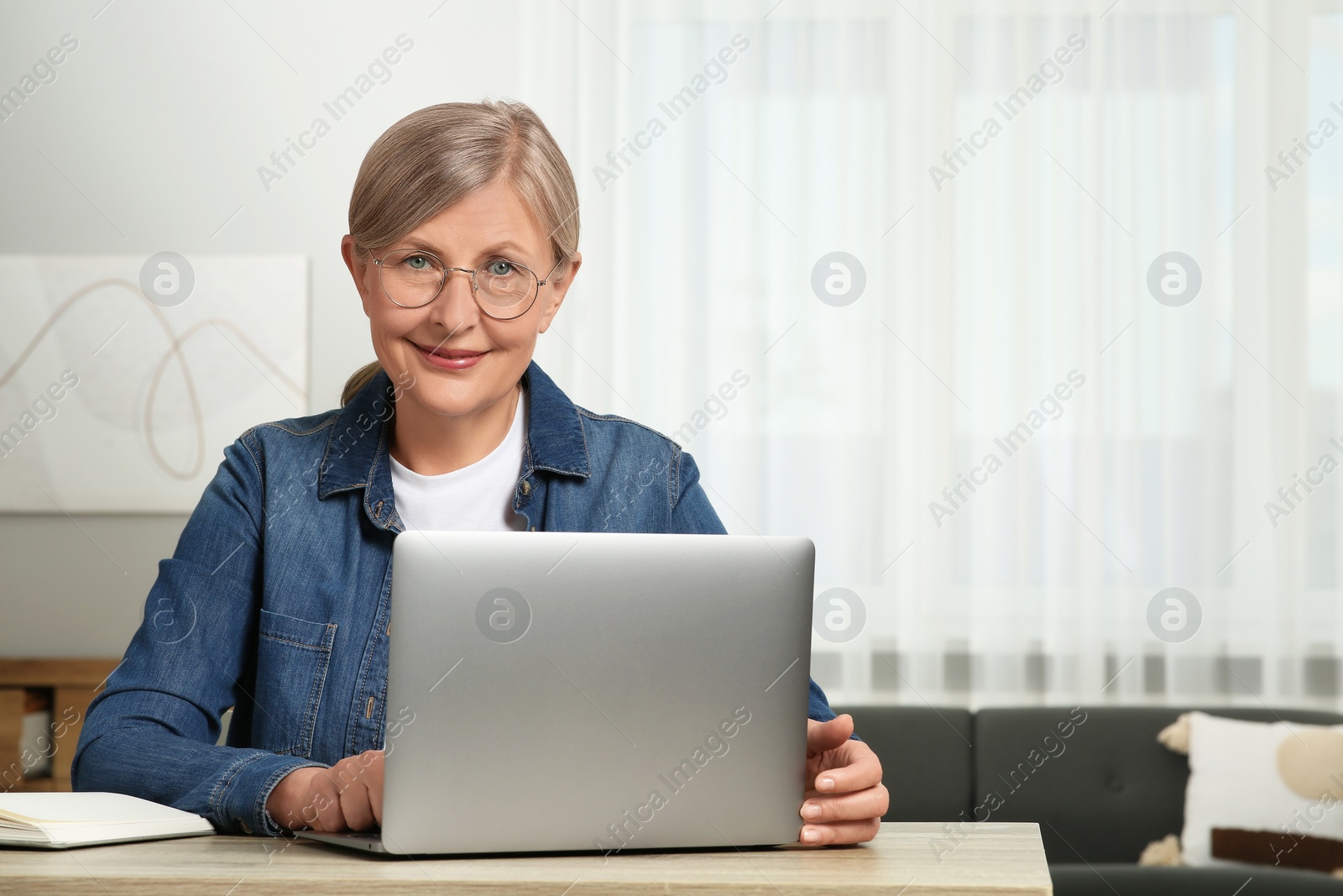 Photo of Beautiful senior woman using laptop at wooden table indoors, space for text