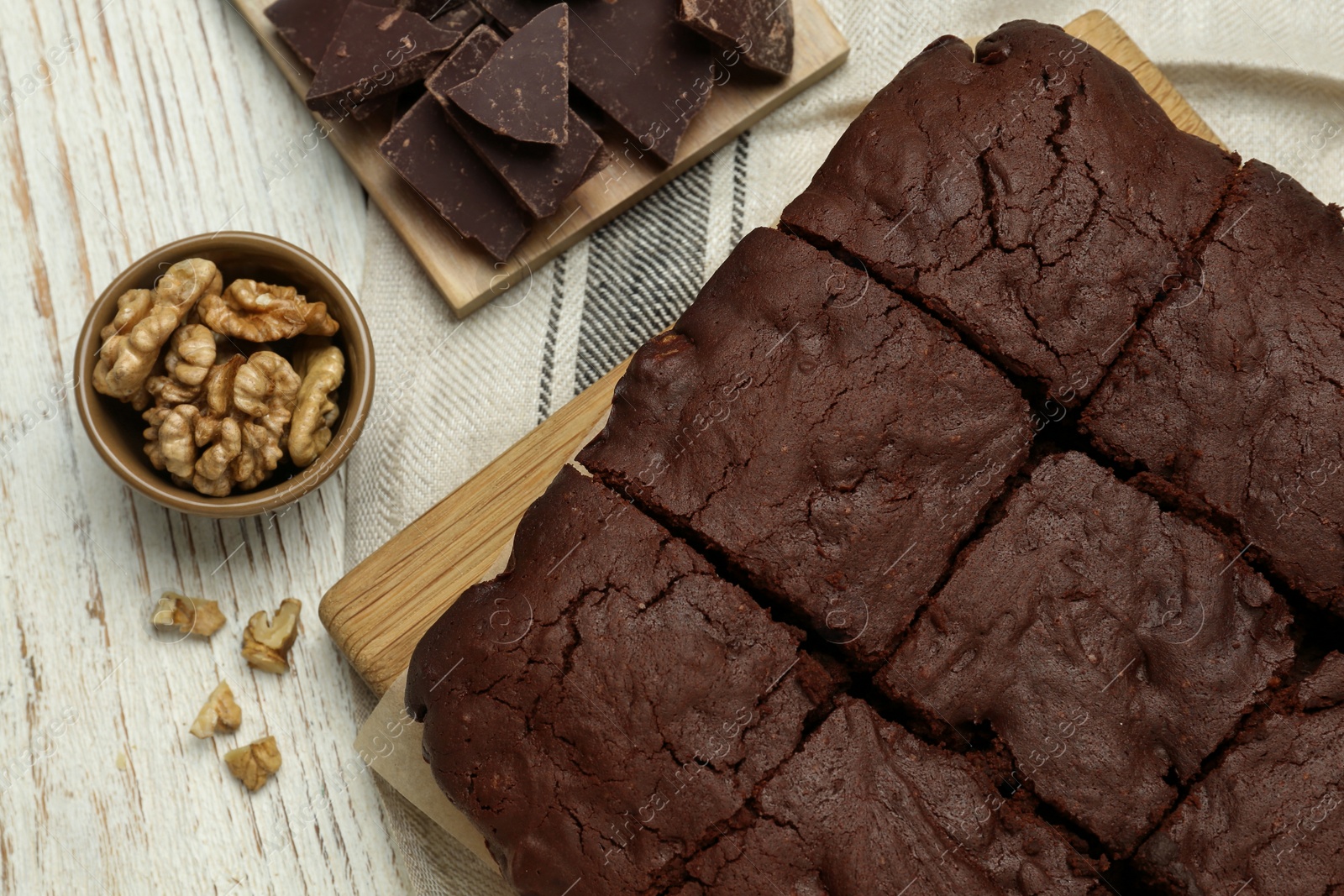 Photo of Delicious freshly baked brownies, walnuts and pieces of chocolate on white wooden table, flat lay