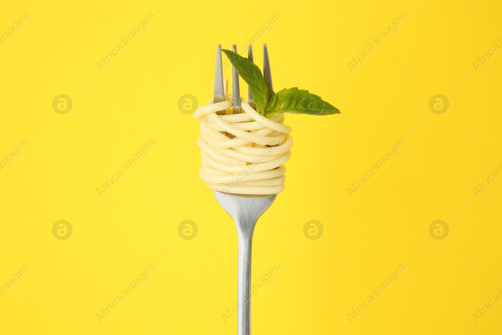 Photo of Fork with tasty pasta and basil leaves on yellow background