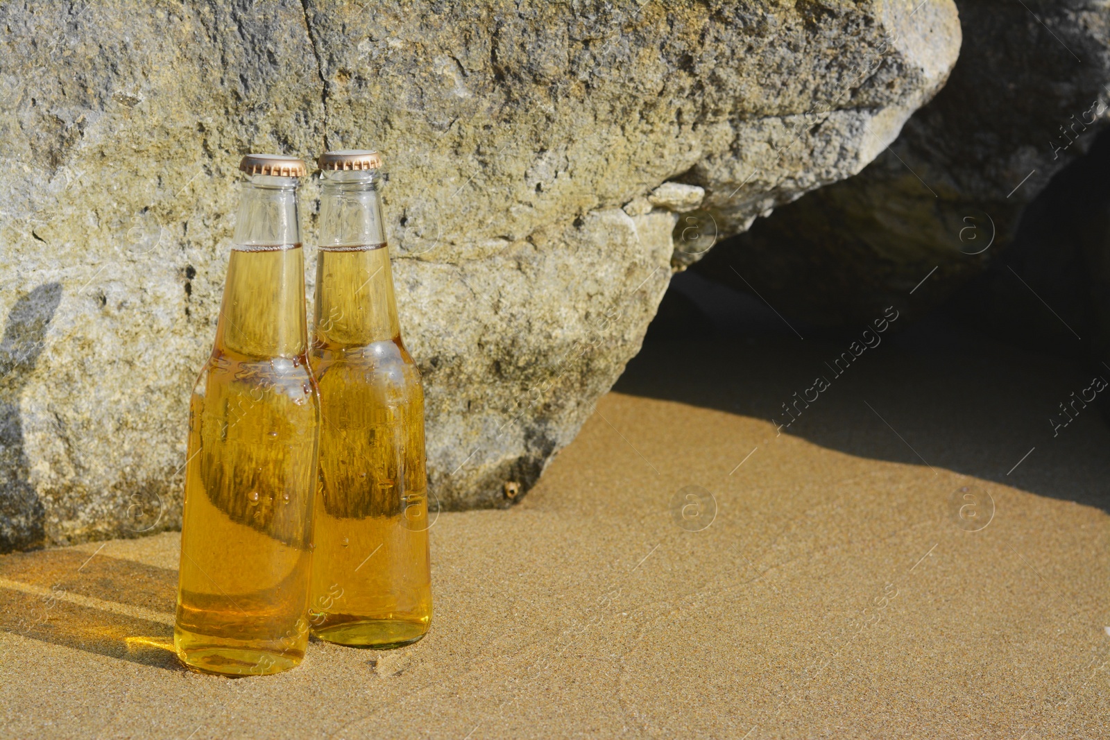 Photo of Bottles of cold beer near rock on sandy beach, space for text