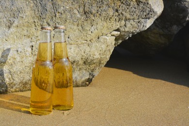 Photo of Bottles of cold beer near rock on sandy beach, space for text