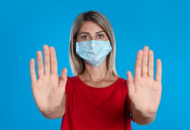Photo of Woman in protective mask showing stop gesture on light blue background. Prevent spreading of coronavirus