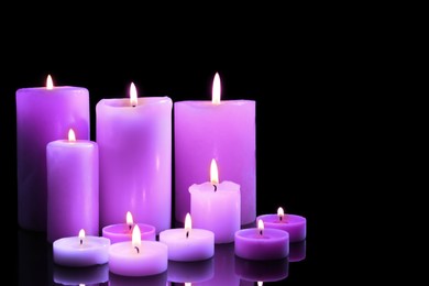 Beautiful burning violet candles on black background. Funeral attributes