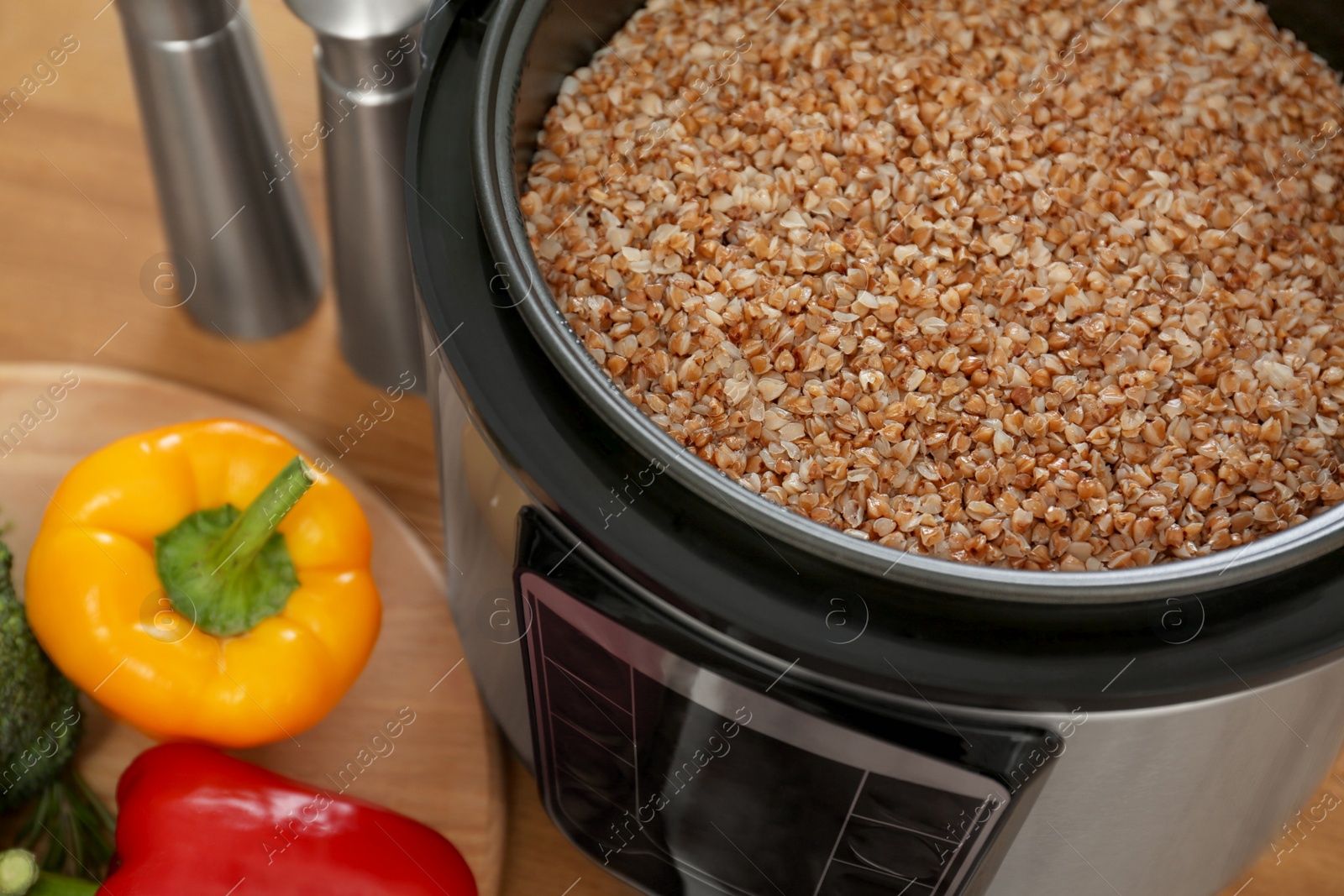 Photo of Delicious buckwheat in modern multi cooker and vegetables on wooden table