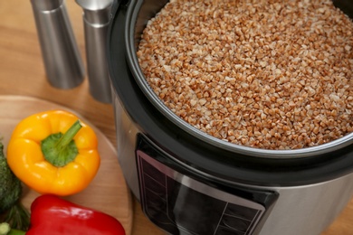 Photo of Delicious buckwheat in modern multi cooker and vegetables on wooden table