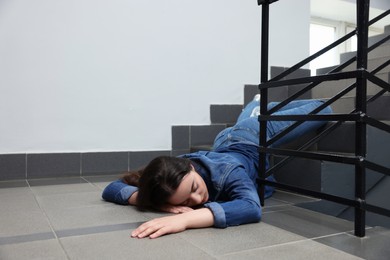 Unconscious woman lying on floor after falling down stairs indoors