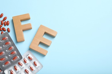 Photo of Wooden letters FE, pills and space for text on light blue background, flat lay. Anemia concept