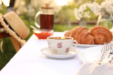 Photo of Stylish table setting with tea and croissants in spring garden