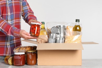 Man taking food out from donation box at light grey table, closeup