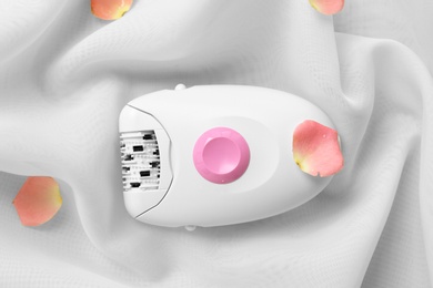 Modern epilator and flower petals on light fabric