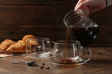 Photo of Woman pouring coffee into glass cup at wooden table, closeup